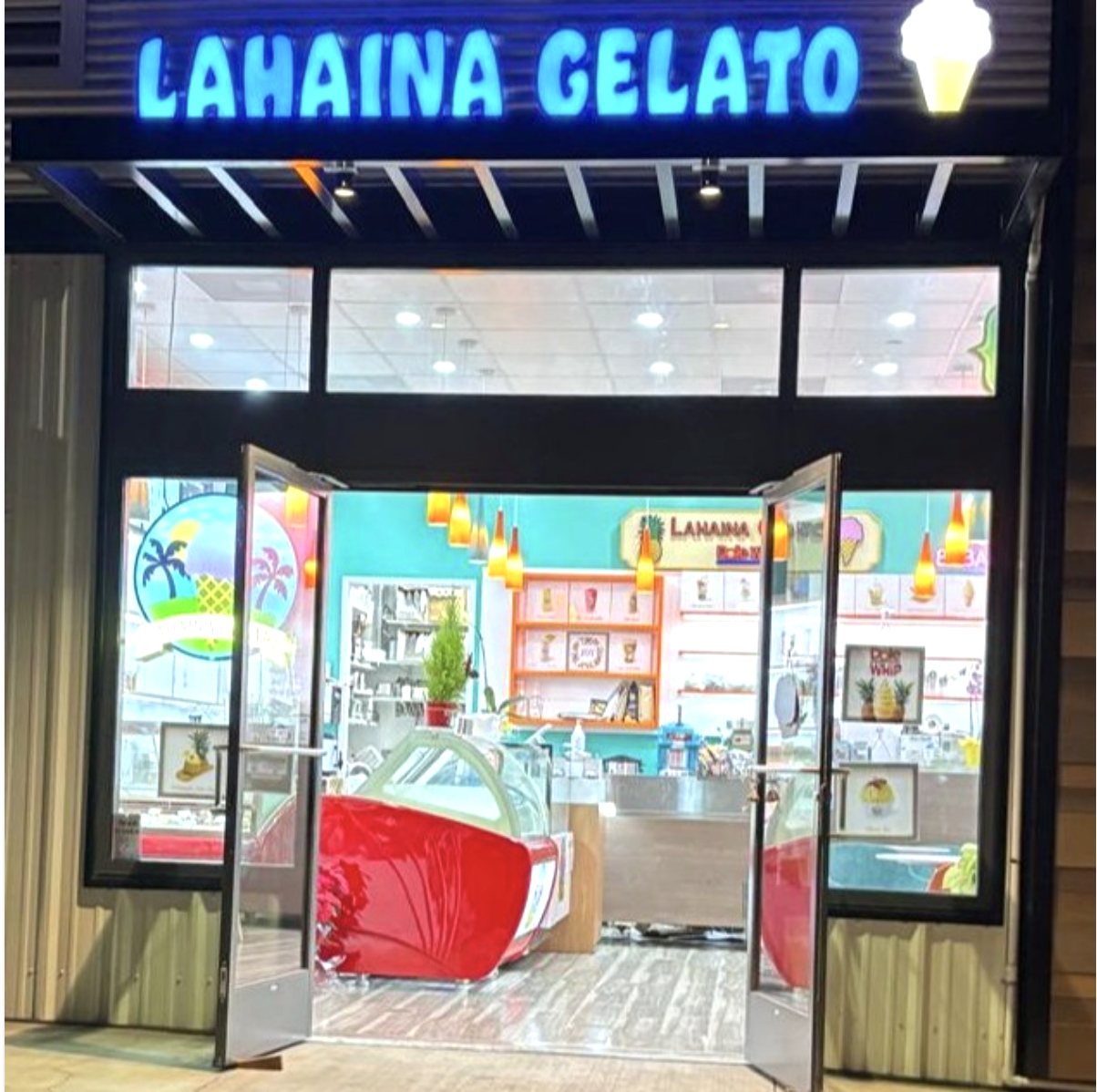 The Lahaina Gelato storefront at night, its blue neon sign lit above open doors, turquoise walls and the red gelato case visible inside
